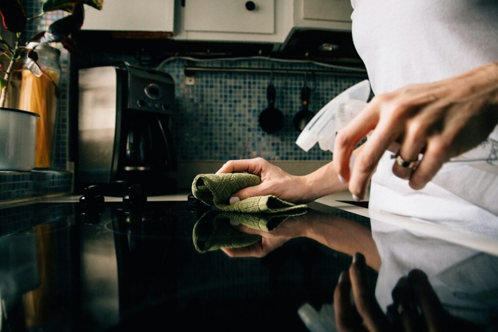 Hands wiping a glass cooktop surface clean in a kitchen