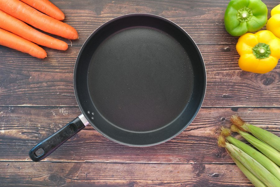 A frying pan beside fresh vegetables on a table